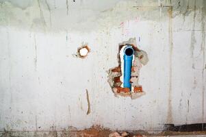 Damaged concrete wall with an exposed blue pipe in hole during major house renovation. Plumbing system work part of construction project with messy background view photo