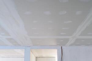 Building interior renovation showing gypsum board ceiling prepared. Smooth plastering applied to edges joints. Electrical wire present. Work creates smooth ceilings, sign of progress photo