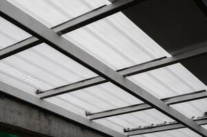 Metal beams supporting translucent sheet roofing. Light filters through corrugated sheet creating patterns. Strong metal framework provides stability shelter overhead. Durable sheet material photo