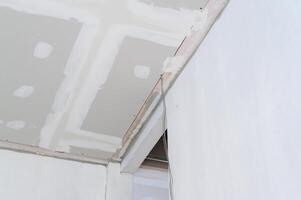 Interior building renovation makes progress on gypsum board ceiling featuring smooth edges. Exposed electrical wire and fresh plastering show ongoing work. sense of anticipation photo