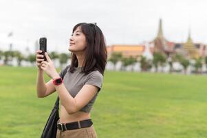 Happy southeast asian woman teenager blogger on solo world travel in Bangkok Thailand take photo with smartphone. An asia tourism concept for local cultural explorer experience