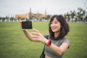 Happy southeast asian woman teenager blogger on solo world travel in Bangkok Thailand take photo with smartphone for local cultural tourism experience concept in Asia for an explorer