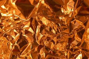 Shimmering golden foil texture with intricate folds and crinkles reflecting light in warm tones photo