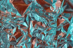 Shimmering crumpled foil creating an abstract texture with vibrant turquoise and orange hues in well lit surroundings photo