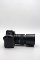 Digital camera with a large lens positioned horizontally on a plain background showcasing its design and features photo