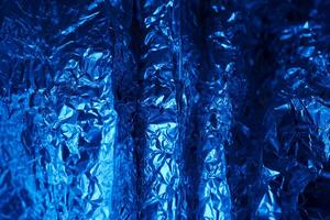 Metallic blue texture showcasing crumpled aluminum foil with intricate patterns and shadows in a vibrant display of light and color photo