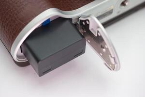 Detailed view of a camera battery compartment opened to reveal a black battery in a vintage styled camera photo