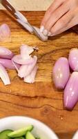A person slices shallots on a wooden board in a well-lit kitchen, showcasing precise knife skills video