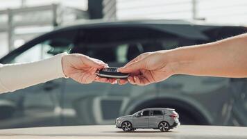 A toy small car drives across the table, and then the seller hands the keys to the buyer after the purchase. Close-up of hands. Finalizing the transaction, buying or leasing a new car. photo