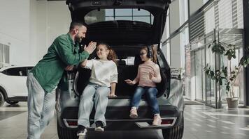 The end of a test drive or purchase of a new, modern car. A happy father with his two daughters sits in the trunk of the car he just bought. The happy family is enjoying the purchase. photo