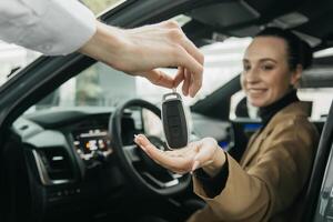 A car dealer hands over the keys to a young woman's car. This is the moment of buying or renting a car. The concept of a deal, lease or expensive purchase photo
