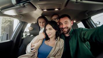 Husband makes a gift to a young wife with two daughters a new car in a modern car dealership. The concept of a successful purchase and happy family life. photo