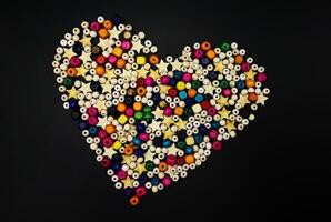 Wooden beads with colorful texture on a yellow background. A decorative accessory for handmade heart-shaped jewelry. A diverse concept of making handicrafts from natural materials. photo