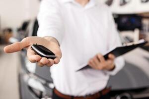 The car dealer hands the car keys towards the camera in a modern dealership. Concept a pivotal moment in the transaction, reflecting the joy and satisfaction of purchasing a car. photo