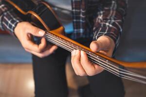 Smiling man gently presses chords on a classic ukulele while seated on a cozy couch. Home photo