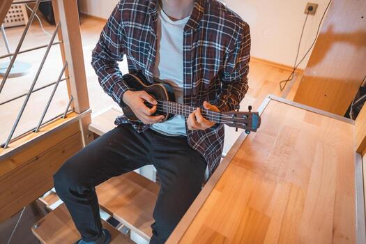 Adult practices a rhythmic pattern on ukulele strings while seated on a couch. photo
