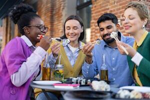 Diverse group of friends enjoying sushi and drinks outdoors, creating a relaxed and joyful dining experience. photo