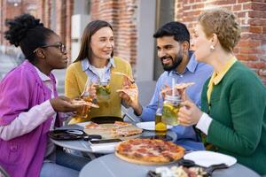 Diverse group of friends enjoying pizza and drinks outdoors, laughing and having a good time together. photo