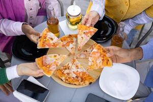 A group of friends enjoying pizza and drinks outdoors, capturing a moment of leisure and shared mealtime. photo