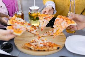 Close-up shot of a group sharing pizza slices, with drinks and a wooden board on the table. photo