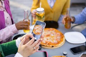 Close-up shot of hands using a phone to take a picture of a pizza during an outdoor gathering with friends. photo