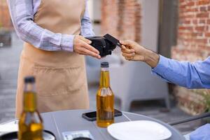 A female waiter at an outdoor cafe processes a credit card payment for a customer at the table using a portable terminal. photo