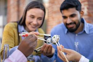 Friends enjoying sushi, using chopsticks, outdoors, capturing a moment of joy and togetherness. photo