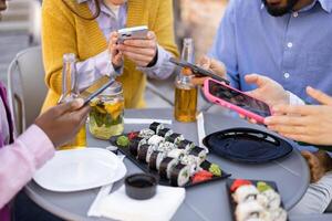 Friends enjoy sushi and drinks while using their phones at an outdoor gathering. photo