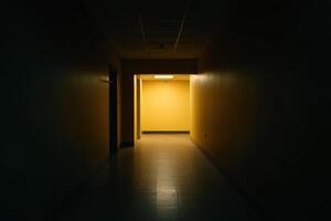 Darkened hallway leads to bright yellow room inside of an unknown Building, an ominous look into the unknown photo