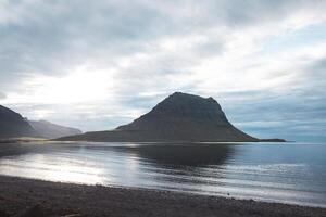 Kirkjufell, the iconic mountain on the Snafellsnes Peninsula in west Iceland, stands majestically with its reflection mirrored in the still waters below, under a soft, pastel sky photo