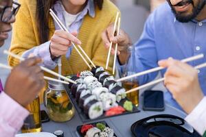 A group of friends enjoys a delicious sushi meal outdoors, using chopsticks to savor various sushi rolls. photo