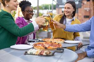 Friends gather outdoors, toasting with drinks and enjoying pizza. A moment of celebration and togetherness captured with smiles and cheer. photo