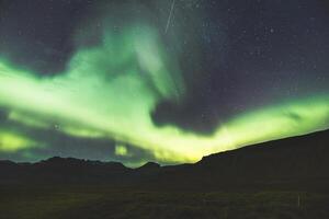 Bright aurora borealis beams arch above rocky summits at midnight. photo