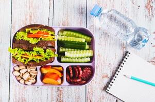 Lunch box with food, bottle of water, notebook and pen on the table top view photo