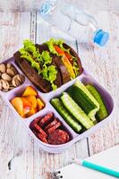 Lunchbox with sandwich, chorizo, cucumber and peach, bottle of water on table vertical view photo