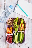 Lunchbox with sandwich, chorizo, cucumber and peach, bottle of water top and vertical view photo