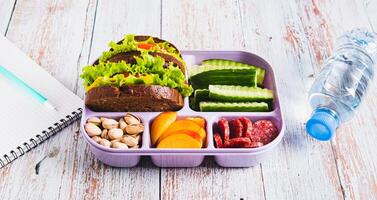 Lunch box with food, bottle of water, notebook and pen on the table web banner photo
