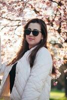 Young woman enjoying springtime under cherry blossom trees during a sunny afternoon in a park setting photo