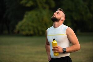 A young fit man with eyes closed listening to music on wireless earbuds and relaxing after a run or workout in the park, active healthy lifestyle, fitness and outdoor exercise concept. photo