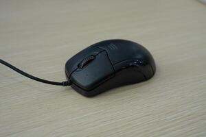A close-up photo of a wired black computer mouse placed on desk. The image suitable for illustrating technology, computer equipment, or workplace themes