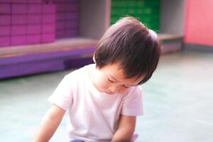 Sleepy boy is forcing himself to play with toys, child doesn't want to take a nap, in an indoor playroom, 2-year-old Asian boy. photo