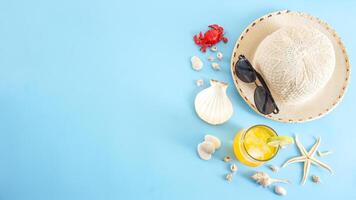 Flat lay composition of summer concept with a glass of cold refreshing summer drink, sunglasses, summer hat, sea shells, starfish, and crab miniature isolated on blue background photo