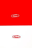 Two paper clips on divided red and white backgrounds offering a contrasting visual statement photo