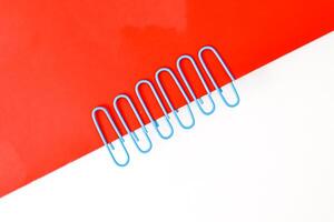 Paper clips in a diagonal arrangement on a divided red and white background create a minimalist design photo