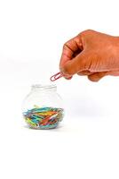 Hand Picking a Red Paper Clip from a Glass Jar Filled with Colorful Clips photo