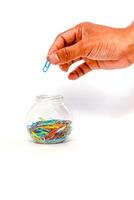 Hand reaching for a colorful paper clip in a jar, against a white background photo