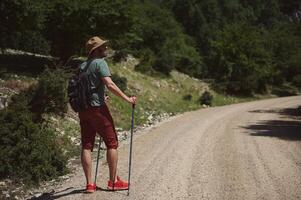 Man Hiking Along a Sunny Mountain Trail with Backpack and Trekking Poles photo