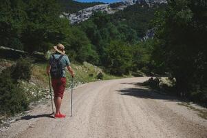 Man Hiking Along a Mountain Path with Walking Sticks and Backpack photo