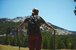 Man Hiking in Scenic Mountain Landscape with Backpack and Trekking Poles, Embracing Outdoor Adventure on a Sunny Summer Day photo