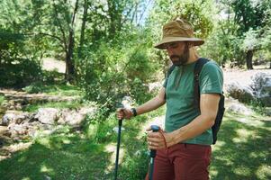 Man Hiking in a Green Forest with Trekking Poles on a Sunny Summer Day photo